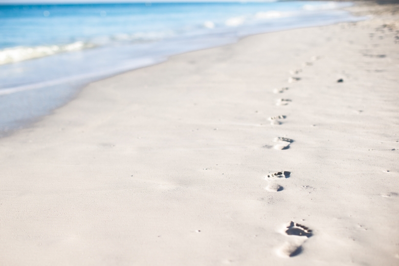 Ein weißer Strand und hellblaues Wasser, Fußabdrücke im Sand.